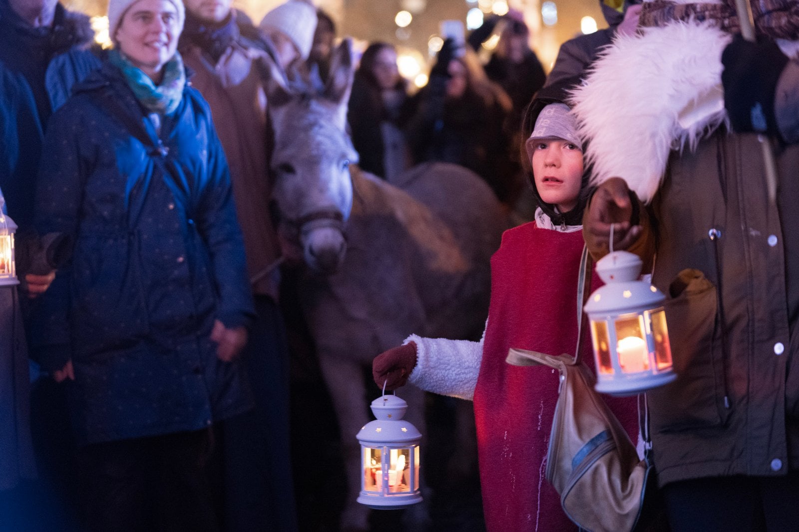 Un enfant en costume de berger porte une lanterne, à côté de l'âne de la crèche vivante