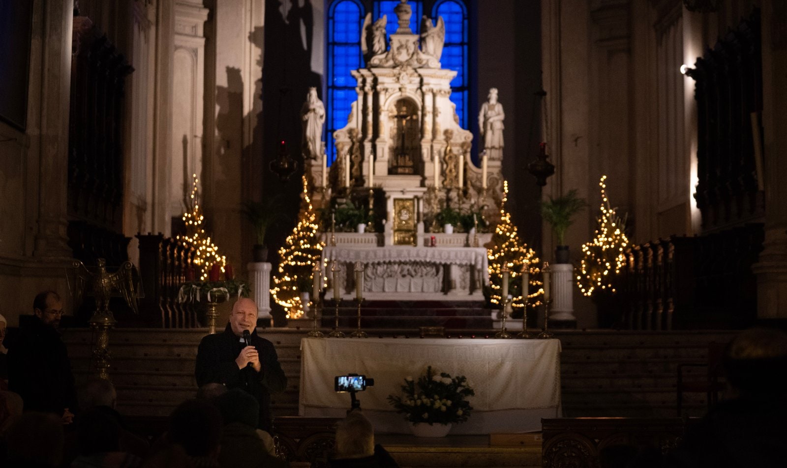 L'intérieur de l'église la nuit : l'autel, des sapins illuminés et un vitrail bleu